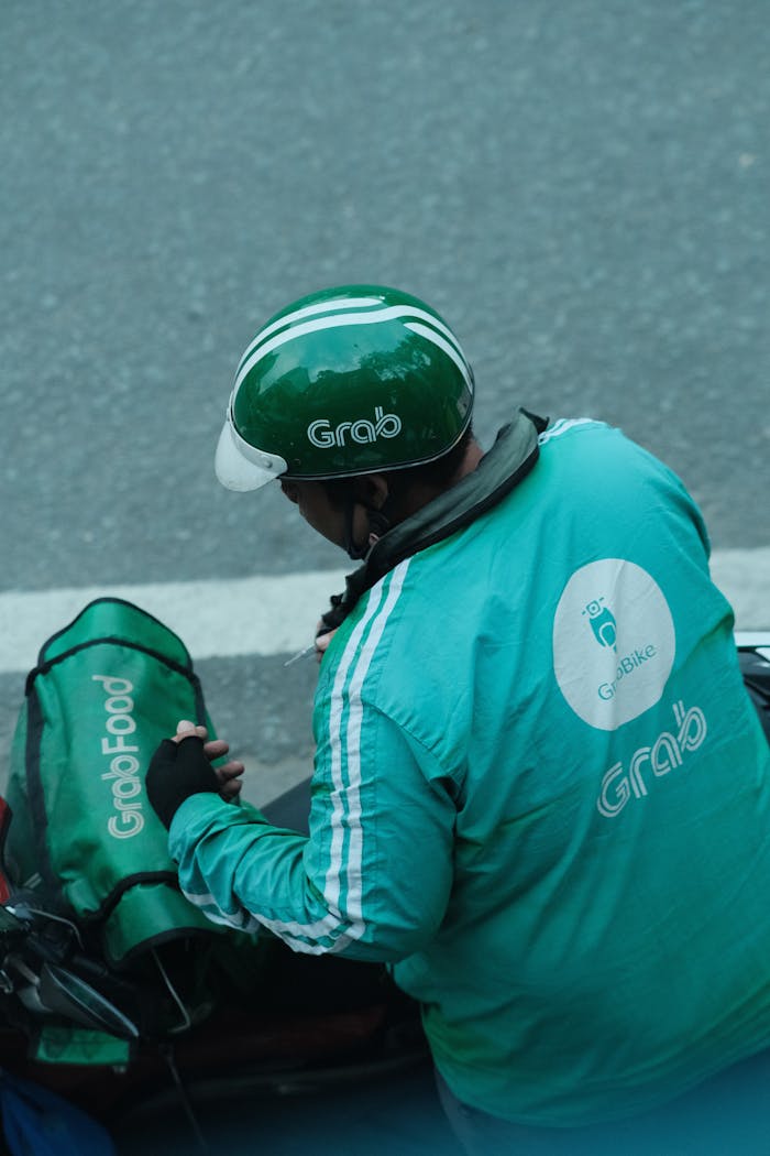A Grab delivery rider in green uniform, preparing for a delivery on a city street.